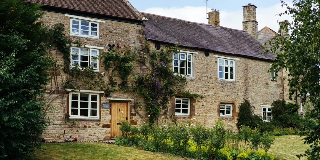 A stone cottage with white windows and climbing plants