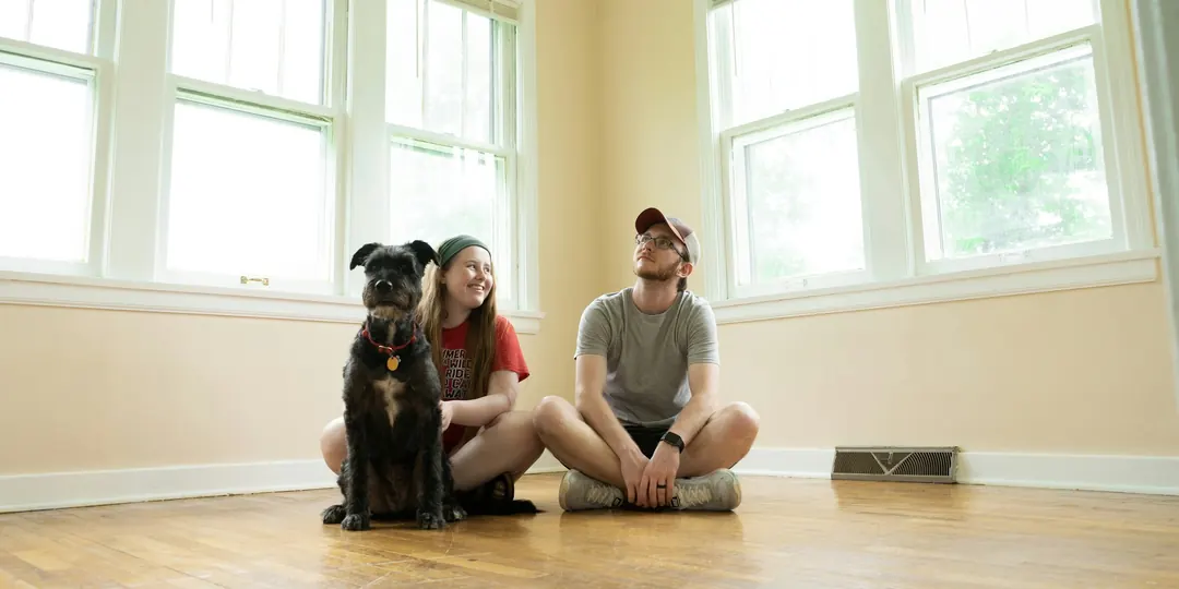 A couple and their dog sitting on the floor of an empty room, imagining their new home