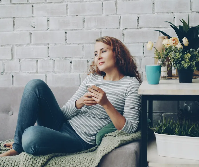 A woman resting at home on the sofa with a coffee