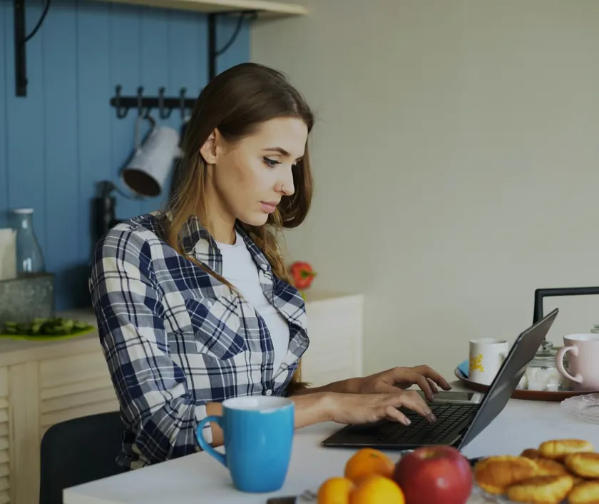 A woman going through her finances on a laptop in her kitchen